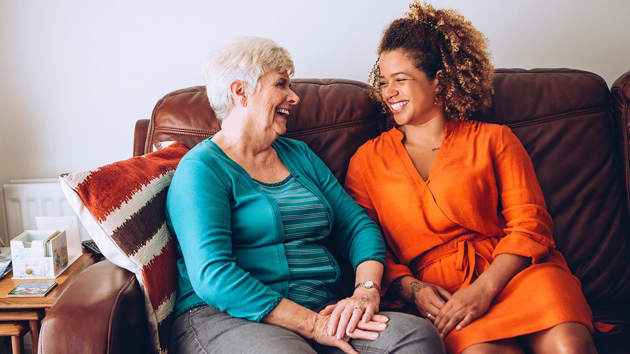 Two women from different generations laughing next to each other on a couch.