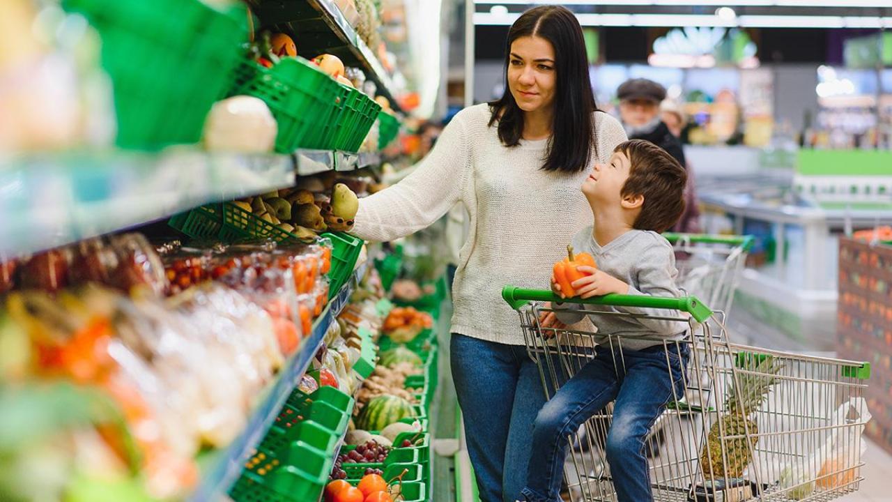 Woman shopping in produce aisle with child in cart.